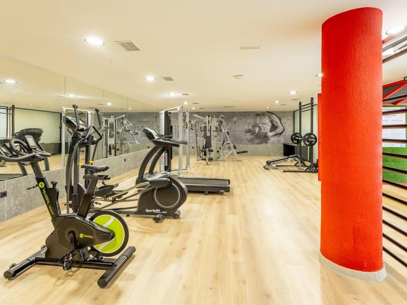 Světelná posilovna s kardio stroji a červenými sloupy v moderním designu.