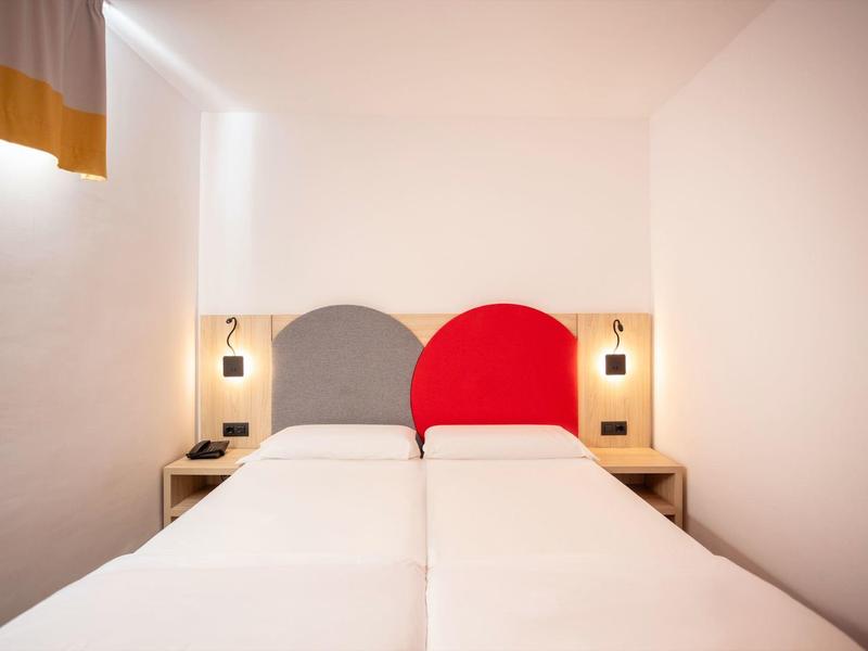 Dvě jednolůžka s barevnými kulatými čely v jednoduchém bílém pokoji