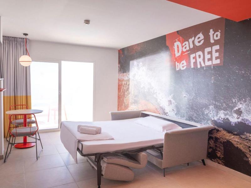 Moderní hotelový pokoj se dvěma postelemi, dekorací stěny a malým posezením s stolem.