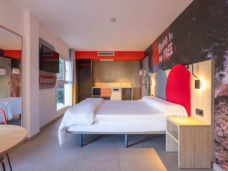 Moderní hotelový pokoj se dvěma postelemi, TV, psacím stolem a červeným osvětlením na zdi.