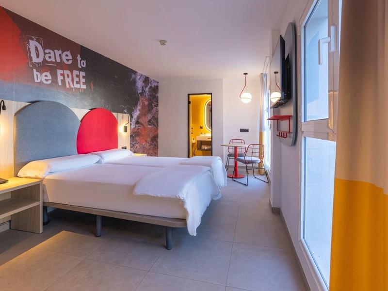 Moderní hotelový pokoj s manželskou postelí, nástěnnou dekorací a přístupem na balkon.