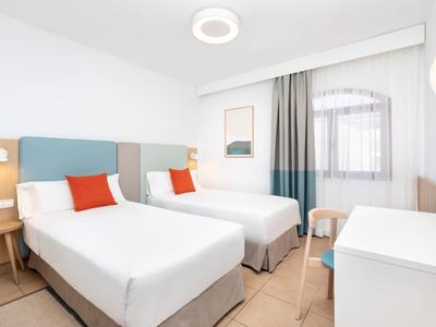 Wohnanlage mit weißen Wänden, grünem Rasen, Palmen und Bergen im Hintergrund unter blauem Himmel.