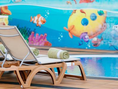 Zwei Liegestühle mit Handtuch am Pool neben einer bunten Unterwasserwand