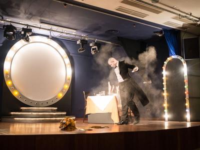 Magicien réalisant un spectacle sur scène avec éclairage dramatique et effets de fumée.