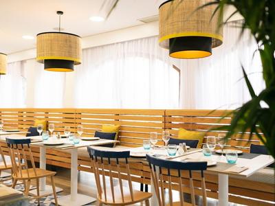 Restaurant lumineux avec mobilier en bois, coussins bleus et grands abat-jours.