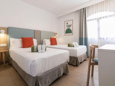 Chambre d'hôtel avec deux lits simples, literie blanche, coussins confortables et une grande fenêtre.