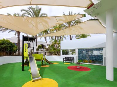 Aire de jeux moderne avec toboggans et voiles d'ombrage, entourée de palmiers.