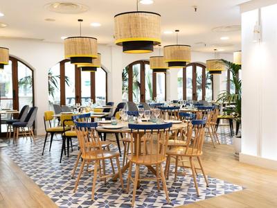 Restaurant lumineux et moderne avec sol à motifs, chaises variées et grands abat-jour.