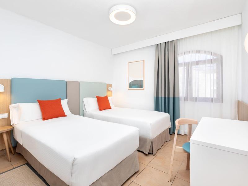 Wohnanlage mit weißen Wänden, grünem Rasen, Palmen und Bergen im Hintergrund unter blauem Himmel.