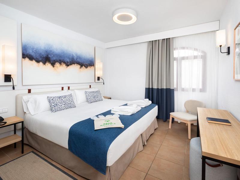 Helles Hotelzimmer mit großem Doppelbett, moderner Kunst und Holzmöbeln.