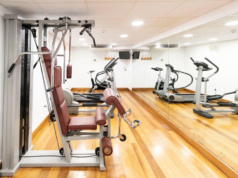 Heller Fitnessraum mit multifunktionalem Trainingsgerät und Cardiogeräten vor großem Spiegel.