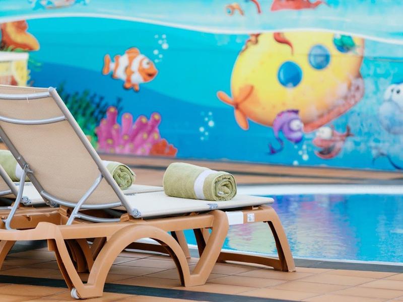 Zwei Liegestühle mit Handtuch am Pool neben einer bunten Unterwasserwand