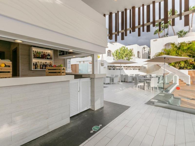 Moderner Outdoor-Barbereich mit weißen und grauen Fliesen und Glasgeländer bei Tageslicht.