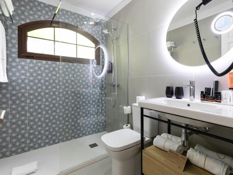 Modernes Badezimmer mit blauer gefliester Duschwand, Toilette und beleuchtetem Spiegel