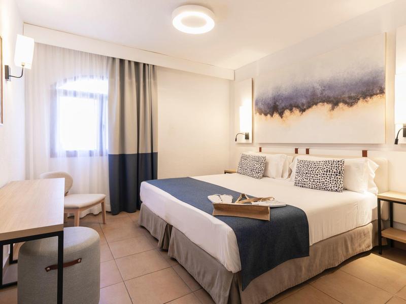 Modernes Hotelzimmer mit großem Doppelbett, Schreibtisch und warmem Licht.