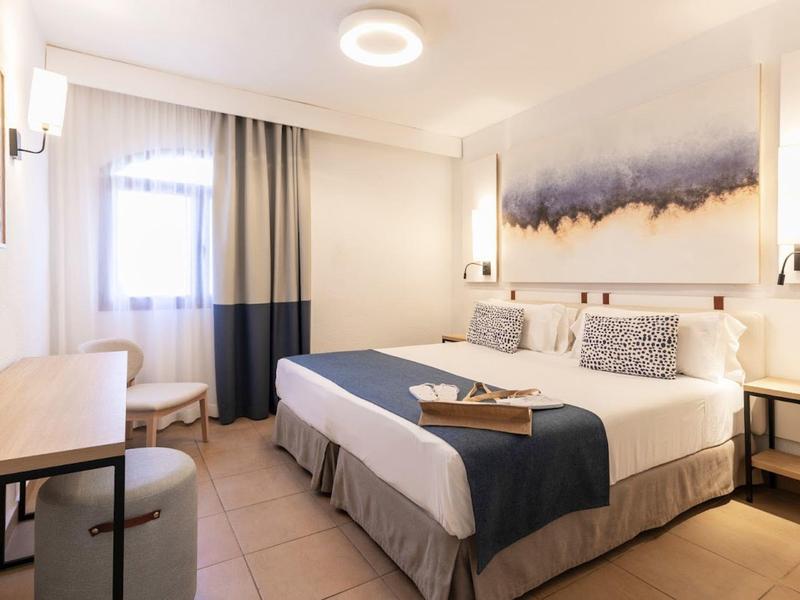 Modern eingerichtetes Hotelzimmer mit Doppelbett, Schreibtisch und Fenster mit Vorhängen.