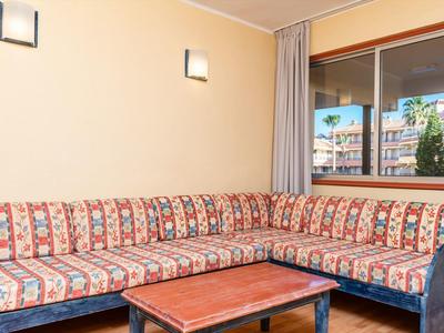 Sala de estar en esquina con sofá estampado y mesa de madera junto a ventana con vista a edificios.