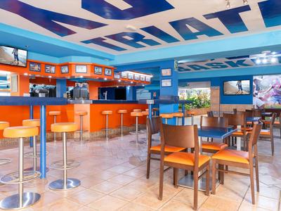 Bar colorida con taburetes naranjas y mesas de madera en un ambiente hotelero animado.