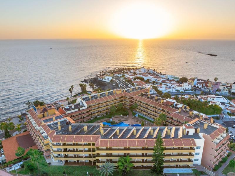 Vista aérea de un complejo hotelero junto al mar al atardecer con piscina y terraza.
