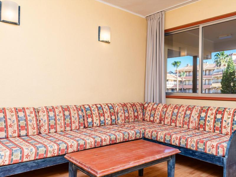 Sala de estar en esquina con sofá estampado y mesa de madera junto a ventana con vista a edificios.