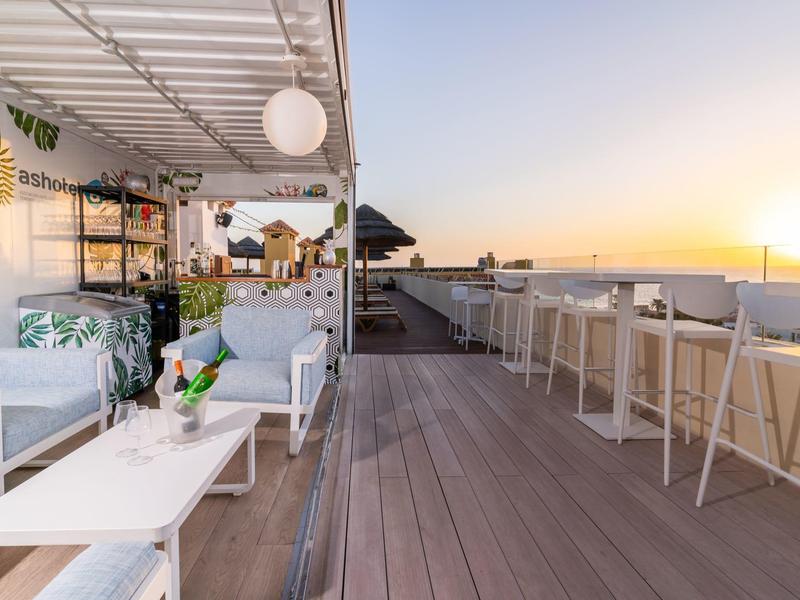 Terraza en la azotea con asientos, mesas y vista al atardecer sobre el mar.
