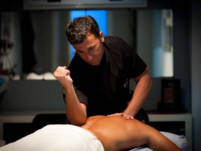 Muž dostává masáž zad v tlumeně osvětlené místnosti na masážním stole.