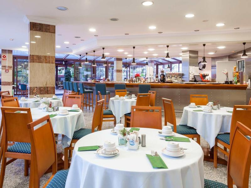 Heller Speisesaal mit runden Tischen, weißen Tischdecken und Holzmöbeln in Restaurantatmosphäre.