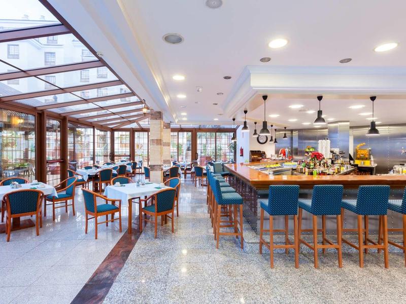 Modernes Restaurant mit blauen Stühlen, großen Fenstern und einer hellen, offenen Raumgestaltung.