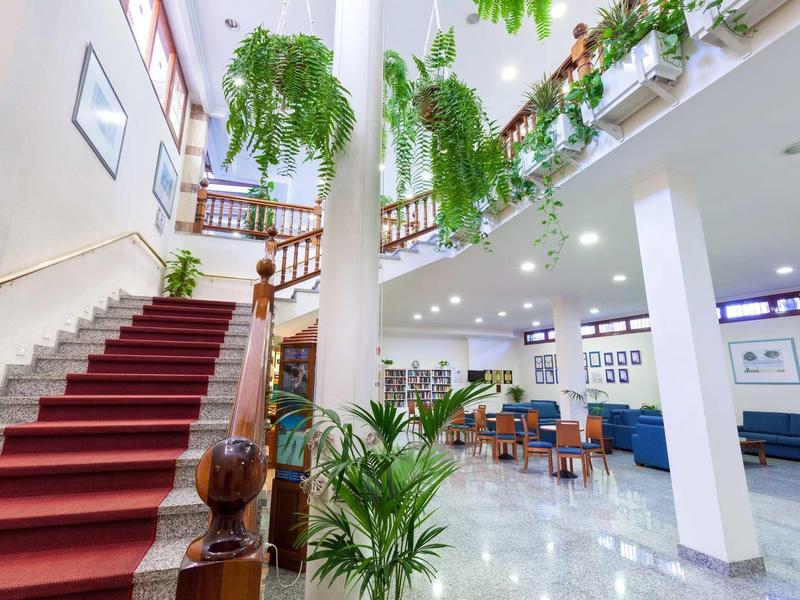 Heller Innenraum mit rotem Teppich auf Treppe, grünen Pflanzen und Sitzbereich mit Tischen und Stühlen.