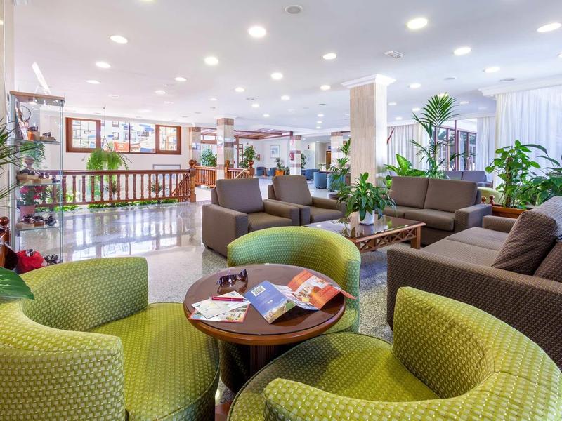 Helles, modernes Wartezimmer mit grünen Sesseln, braunen Sofas, Pflanzen und runden Tischen.