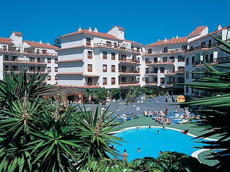 Große Wohnanlage mit Pool, Sonnenliegen und Palmen vor blauem Himmel.