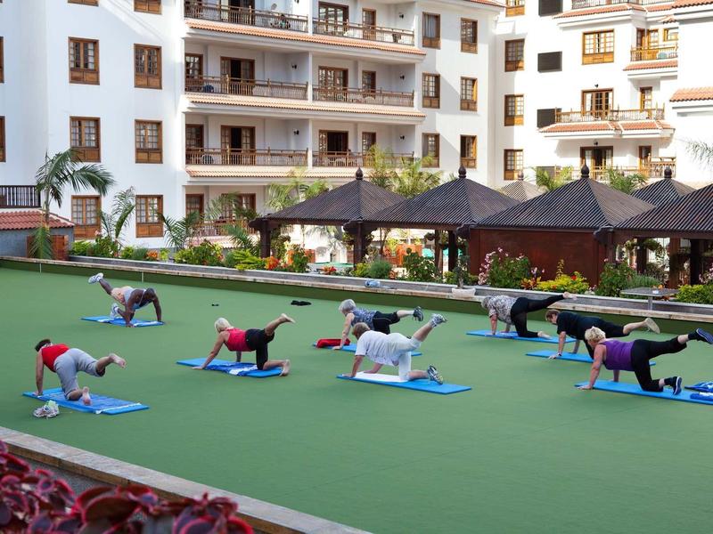 Menschen trainieren draußen auf Yogamatten auf einer Rasenfläche vor einem Wohngebäude.
