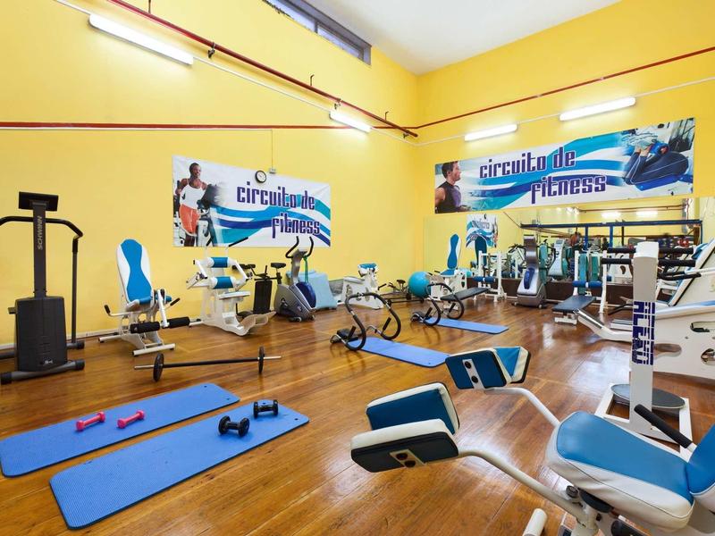 Hellgelber Fitnessraum mit Holzboden, Trainingsgeräten und blauen Matten auf dem Boden.