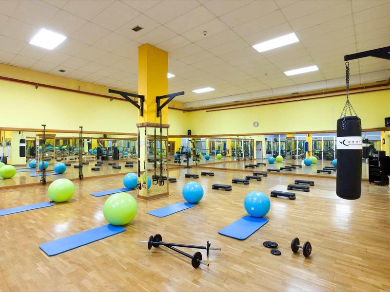 Großer Fitnessraum mit Holzboden, Spiegelwand, Matten, Hanteln, Gymnastikbällen und Boxsack.