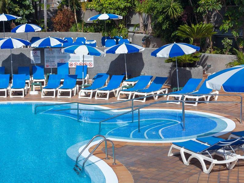 Leerer Poolbereich mit blauen Liegestühlen und blauen-weißen Sonnenschirmen im Außenbereich.