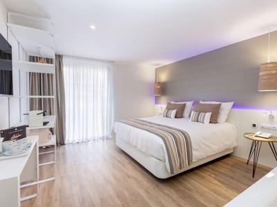 Chambre d'hôtel moderne avec lit double, sol en bois et grande fenêtre avec rideaux.