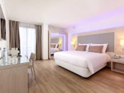 Chambre d'hôtel lumineuse avec grand lit, bureau et sol en bois.