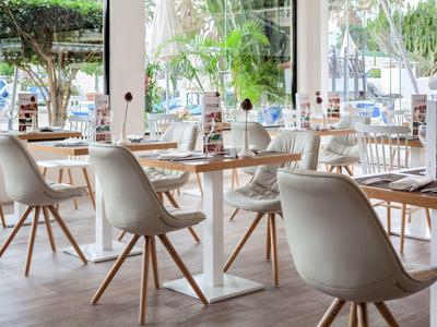 Restaurant lumineux et moderne avec des chaises blanches et des tables en bois, entouré de grandes fenêtres.