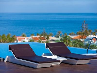 Deux chaises longues au bord d'une piscine à débordement avec vue sur la mer et les palmiers.