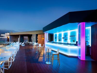 Espace bar extérieur moderne d'hôtel avec comptoir éclairé et chaises blanches au crépuscule.