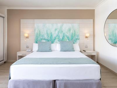 Chambre d'hôtel moderne avec lit double, murs clairs et tête de lit décorative à motifs végétaux.