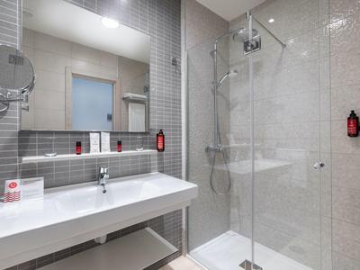 Salle de bain moderne avec grand miroir, lavabo et douche à l'italienne avec cloison en verre.