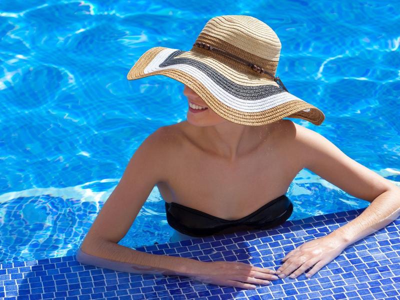 Femme avec grand chapeau de soleil se détend au bord d'une piscine bleue.