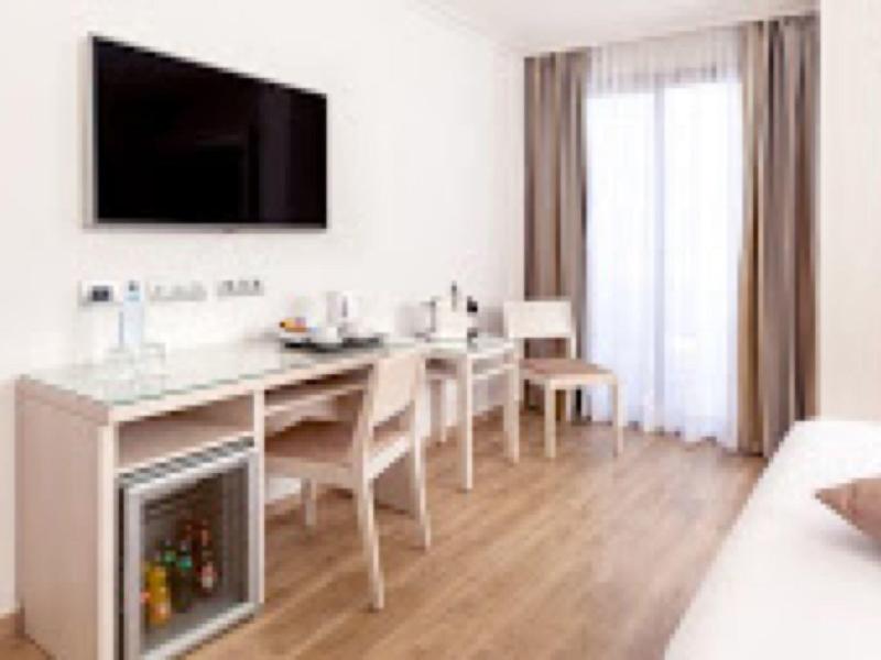 Chambre d'hôtel lumineuse avec bureau, chaises, minibar et télévision murale.