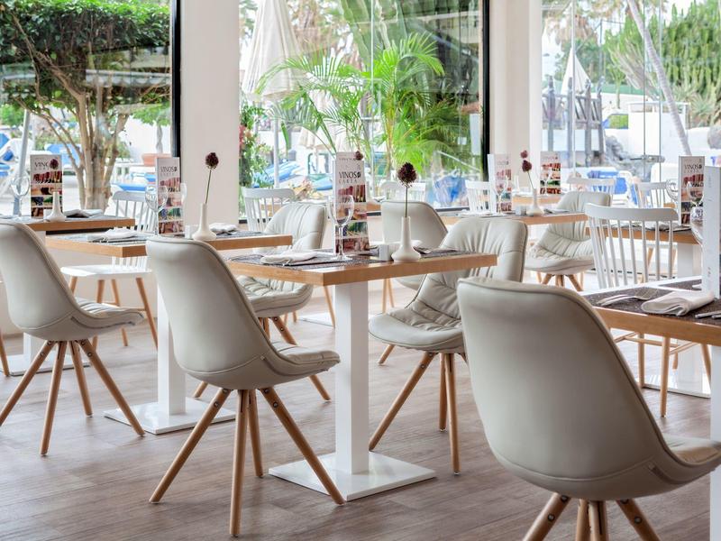 Restaurant lumineux et moderne avec des chaises blanches et des tables en bois, entouré de grandes fenêtres.