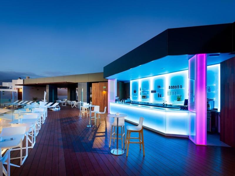 Espace bar extérieur moderne d'hôtel avec comptoir éclairé et chaises blanches au crépuscule.