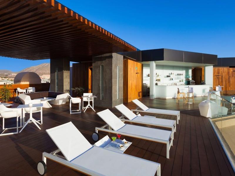 Terrasse sur le toit moderne avec chaises longues, espace salon et bar sous un ciel clair