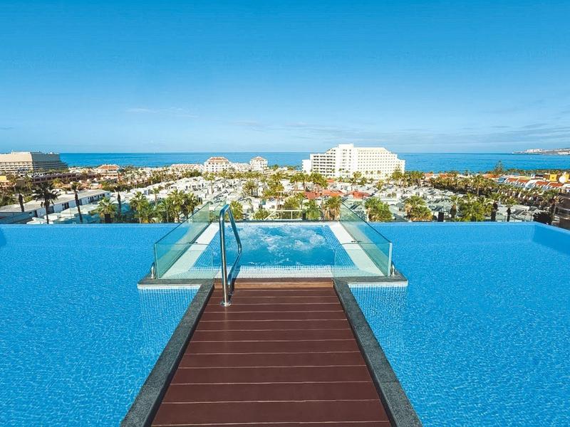 Piscine à débordement avec vue sur la ville et la mer par une journée claire.