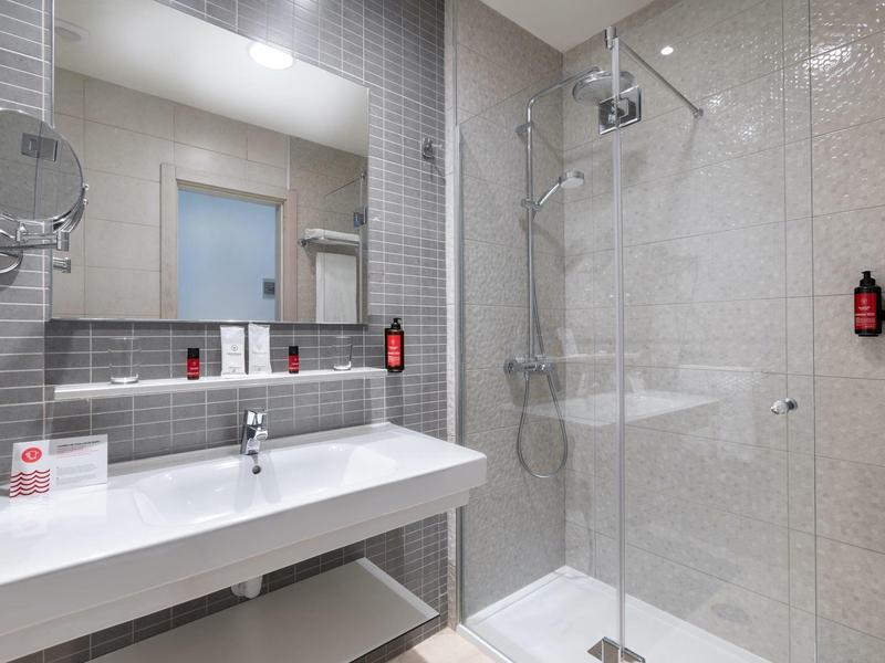 Salle de bain moderne avec grand miroir, lavabo et douche à l'italienne avec cloison en verre.