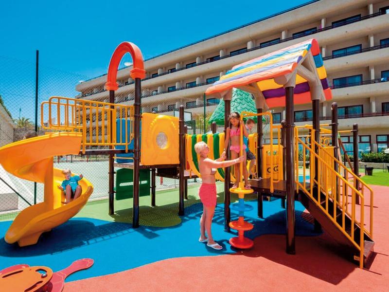 Kolorowy plac zabaw dla dzieci ze zjeżdżalnią i rusztowaniem obok nowoczesnego budynku hotelowego w słońcu